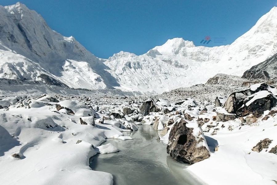 Frozen mountain lake surrounded by snow-covered rocks with towering Himalayan peaks in the background